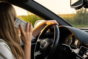 Happy young woman speaking by mobile phone while driving car. Business woman talking phone call in automobile. Unsafely risky driving. Concept of multitasking photo