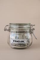 Saving Money In Glass Jar filled with Dollars banknotes. PENSION transcription in front of jar. Managing personal finances extra income for future insecurity. Beige background photo