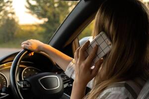 Happy young woman speaking by mobile phone while driving car. Business woman talking phone call in automobile. Unsafely risky driving. Concept of multitasking photo