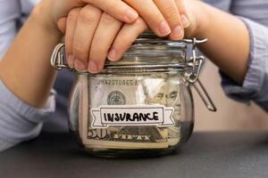 Unrecognizable woman holding Saving Money In Glass Jar filled with Dollars banknotes. INSURANCE transcription in front of jar. Managing personal finances extra income for future insecurity background photo