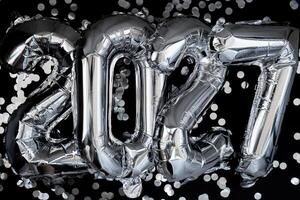 Happy new year 2027 metallic balloons with confetti on dark black background. Greeting card silver foil balloons numbers Christmas holiday concept. Celebration party congratulation decoration photo