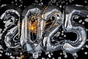 Happy new year 2025 metallic balloons with confetti and sparkler firework Bengal lights on dark black background. Greeting card silver foil balloons numbers Christmas holiday concept. Celebration party congratulation decoration photo