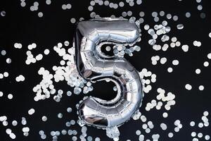 5 five metallic balloon with sparkling confetti on dark black background. Greeting card silver foil balloon number Happy birthday holiday concept. Copy space for text. Celebration party congratulation decoration photo