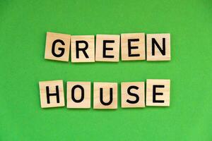 Green house text on wooden blocks on green background. Ecological concept Sustainable responsible living. Copy space. Single word photo