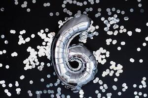 6 six metallic balloon with sparkling confetti on dark black background. Greeting card silver foil balloon number Happy birthday holiday concept. Copy space for text. Celebration party congratulation decoration photo