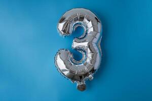 3 three metallic balloon isolated on blue background. Greeting card silver foil balloon number Happy birthday holiday concept. Copy space for text. Celebration party congratulation decoration photo