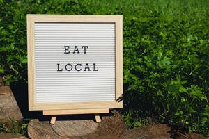 Letter board with text EAT LOCAL on background of garden bed with green herb parsley. Organic farming, produce local vegetables concept. Supporting local farmers. Seasonal market photo