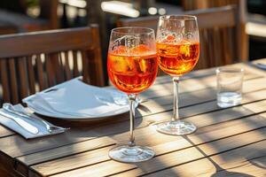 Two glasses of Aperol Spritz with ice on a wooden table, outdoor setting with soft shadows. photo