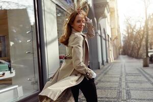 espalda ver de sonriendo de moda mujer en Saco cruce el ciudad calle y mirando a cámara foto