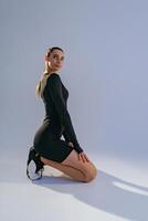 Portrait of woman wearing sportswear sitting floor on studio background and looking at camera photo