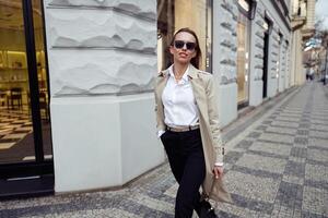 Happy fashionable woman in sunglasses standing on city street background and looking at camera photo