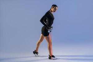 Strong woman in sportswear performs fitness exercises with resistance band on studio background photo