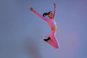 Smiling sporty woman in sportswear jumping on studio background. Sport and healthy lifestyle photo