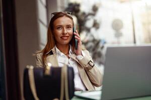 sonriente europeo mujer de negocios hablando teléfono mientras trabajando en línea sentado a al aire libre café terraza foto