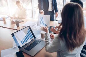 Close up of business people consider documents with graphs and charts using laptop in office photo