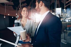 Smiling office employees drinking coffee and discussing work issues using tablet in office photo