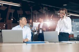 Smiling business woman sitting on table and talking phone with client in modern office photo