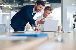 Smiling office worker shows his creative project mature female businesswoman on laptop photo