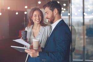 Positive office employees drinking coffee and discussing work issues using tablet in a office photo