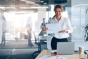 Positive mature businesswoman showing her new plans with graph in modern office photo