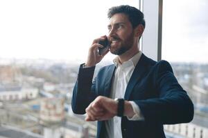 sonriente empresario mirando fuera el ventana y hablando en un móvil teléfono con un cliente foto