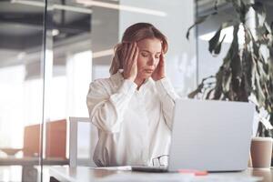 Confident businesswoman working on laptop at her workplace at modern office.Headache concept photo