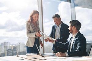 Positive office employees discussing work issues using laptop and documents with graphs and charts photo