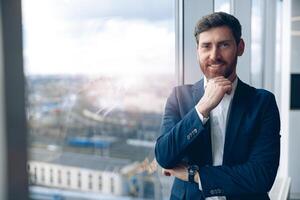 Portrait of a attractive smiling businessman standing near window in a modern office photo