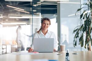 Portrait of smiling lady boss working on laptop at her workplace at modern office photo