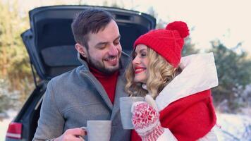 Young couple, a man and a woman hugging near the car in a winter and drinking coffee, snowy forest video