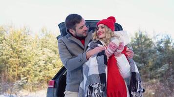 Young couple, a man and a woman hugging near the car in a winter and drinking coffee, snowy forest video