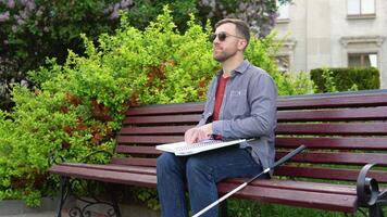 Young blind man sitting on bench in city park and reading a braille book video