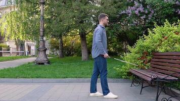 A blind man with a cane approaches the bench and sits down video