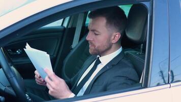 portret van een zelfverzekerd Mens zittend in een auto met documenten in een bedrijf pak in de buurt een modern kantoor gebouw video