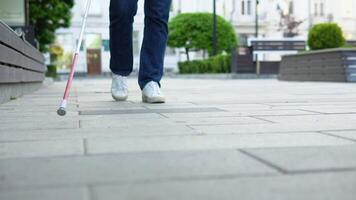 Young blind man with using safety stick for walking alone outdoors. Male person wearing glasses and casual clothes. Independence concept video