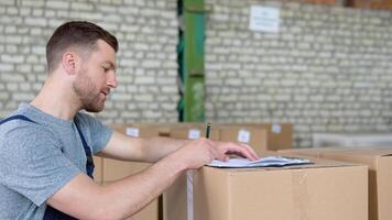 Delivery man writing something to clipboard. Courier checks the parcels on warehouse video