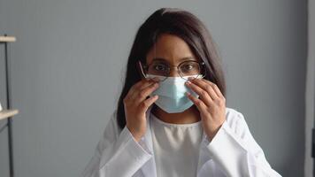 Young indian female doctor puts on a protective blue mask. Virus protection video