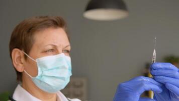 Senior female doctor in a protective mask with a vaccine syringe in his hands video