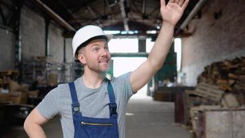 Serious manager in helmet and uniform giving commands to workers on industrial warehouse. Bearded man gesturing and shouting during working process video