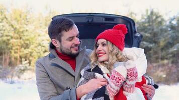 jovem casal, uma homem e uma mulher abraçando perto a carro dentro uma inverno e bebendo café, Nevado floresta video