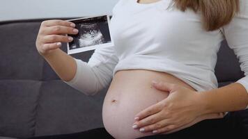 A pregnant woman strokes her tummy and shows a photo of the ultrasound diagnosis of the fetus video