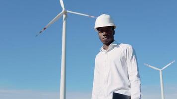 African American electrician engineer standing on the background of a windmill at an air power plant. Wind power turbines generating clean renewable energy video