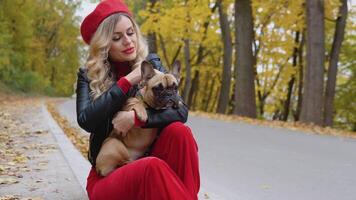 Beautiful blonde woman in a red suit holding a french bulldog in her arms video