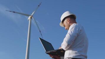 A male engineer in a white helmet and a classic shirt inspects the power plant's capacity and makes notes in a laptop video