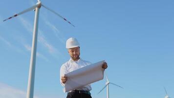 A male engineer in a white helmet and a classic shirt inspects the power plant's capacity and reads project drawings on a large sheet of paper video