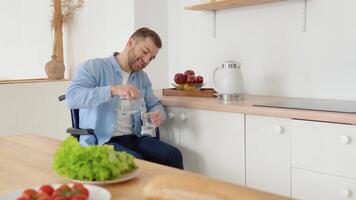 alegre discapacitado persona en un silla de ruedas vierte agua dentro un vaso en el cocina video