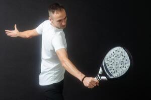 Portrait of man playing paddle tennis in position to hit a backhand ball black isolated background. Front view. photo