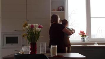 mamma håller på med hushåll sysslor i de kök med en bebis i henne vapen, tillbaka se video