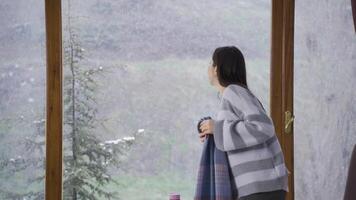 Asian young woman watching snowfall through window. video