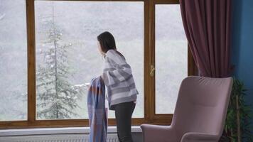 Young asian woman watching the falling snow looking out the window. video